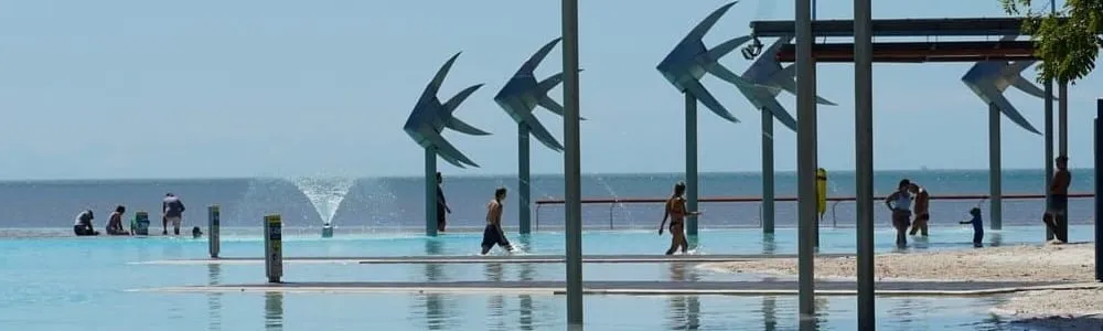 Swimmers at the Cairns Esplanade lagoon, with the Woven Fish sculptures standing over the water